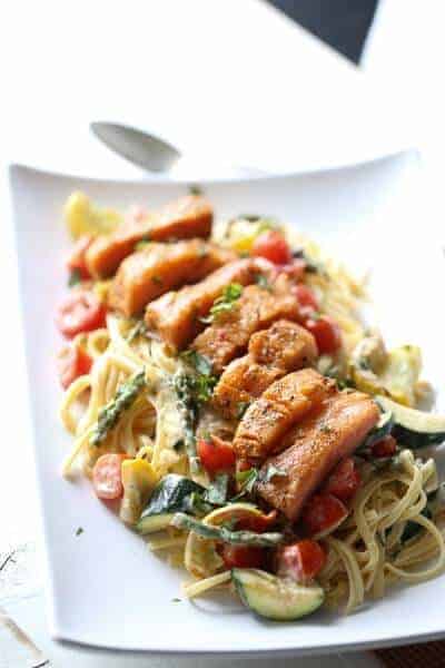 This salmon topped pasta Primavera is filled with veggies and tossed with a light, creamy sauce. A simple, elegant meal for any occasion. lemonsforlulu.com