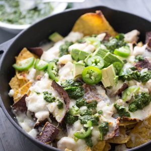 Loaded Nachos Brazilian Style! These nachos are topped with both pork and chicken, lots of cheese, creamy avocados and a homemade chimichurri sauce!