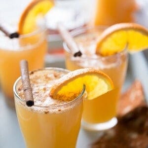 Three beer glasses of simple ginger beer with sliced oranges and cinnamon sticks.