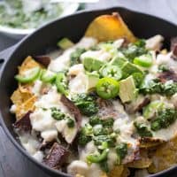 Loaded Nachos Brazilian Style! These nachos are topped with both pork and chicken, lots of cheese, creamy avocados and a homemade chimichurri sauce!