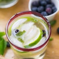 One glass of delicious Champagne Blueberry Mojitos on a wooden platter.
