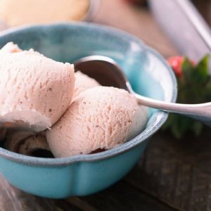 Three scoops of Delicious Brown Sugar Strawberry Ice Cream in a blue bowl on a wooden table.